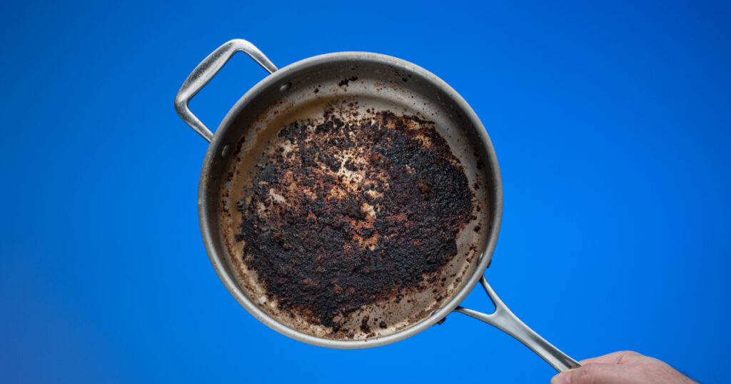 Dirty oily burnt metal frying pan held in hand by male hand.
