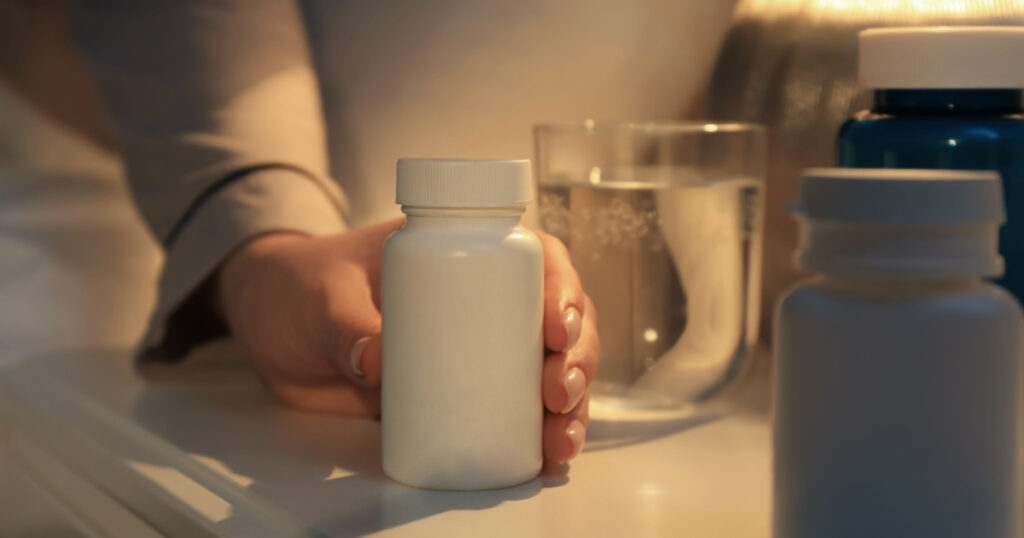 Woman taking pills from nightstand indoors, closeup. Insomnia treatment