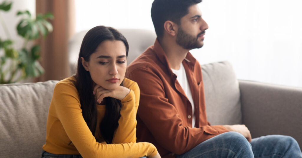 Marital Crisis. Unhappy Arabic Couple Sitting On Couch At Home, Having Relationship Problems. Bad Marriage, Breakup Concept. Selective Focus On Frustrated Woman