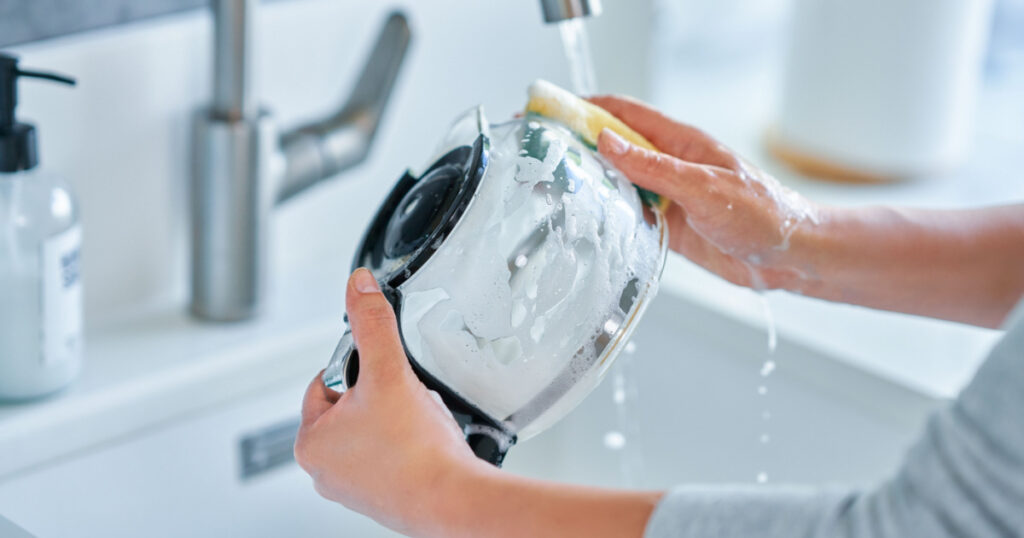 Young woman cleaning coffee pot or machine
