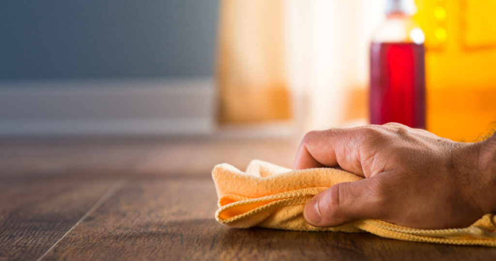 Male hand applying wood care products and cleaners on hardwood floor surface.