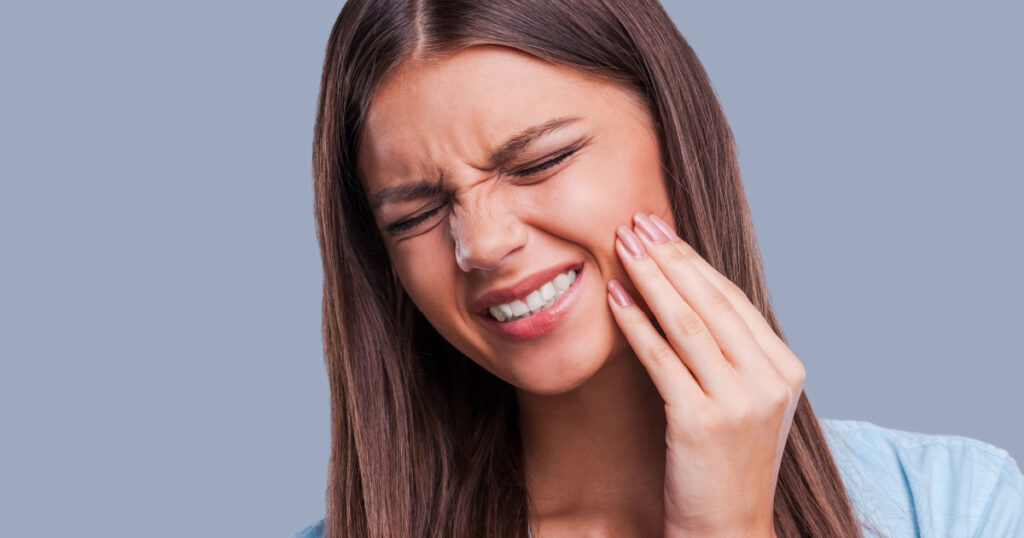 Suffering from toothache. Beautiful young woman suffering from toothache while standing against grey background