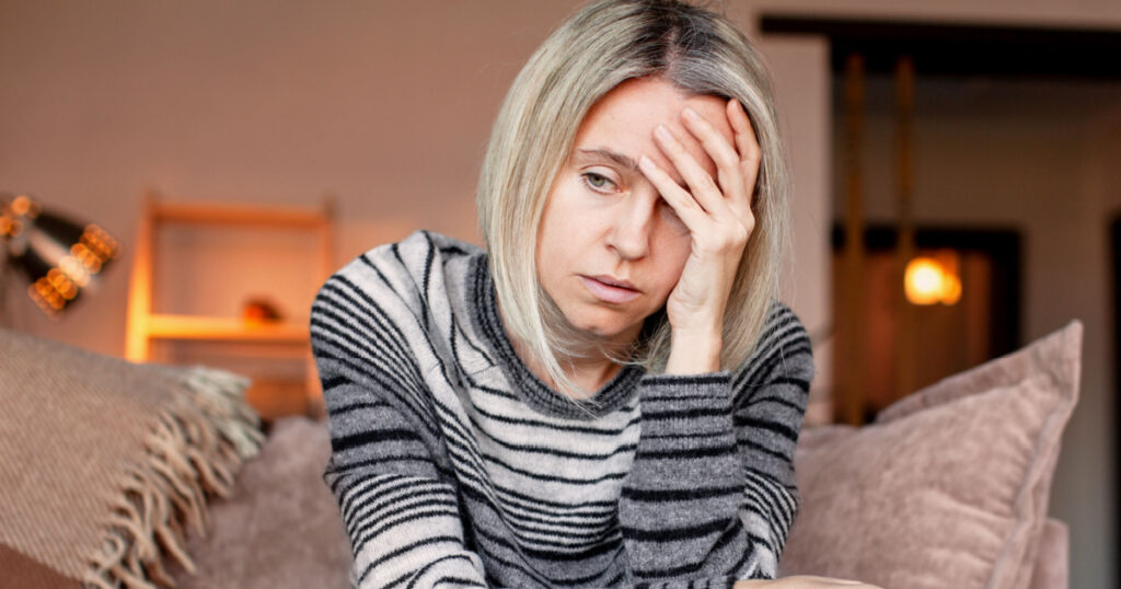 Stressed middle aged woman sit on sofa in living room, lost in thought. Depressed lady at home
