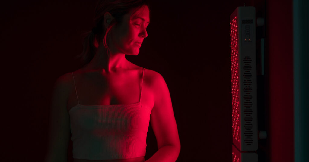 Mature woman receiving red light therapy. Woman standing next to a red light device in a beauty spa. Anti-aging and skin care treatment.