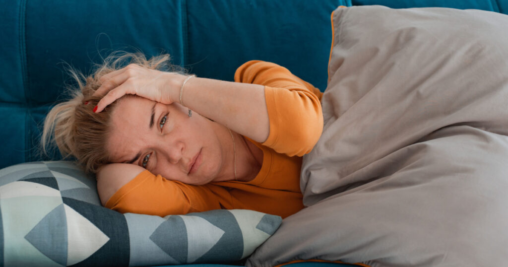 depressed mature woman lying sofa with her arms around herself, covering her head with hands, unhappy woman suffering from insomnia depression, psychological problem, concept impotence, asthenia