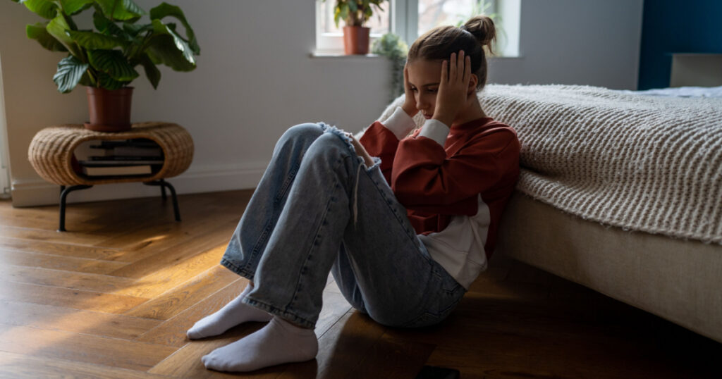 Frustrated sad teen girl child sitting alone on floor being bullied online, having feelings of isolation and fear. Depressed teenage kid holding head in hands dealing with first love heartbreak