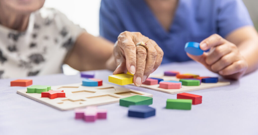 Caregiver and senior woman playing wooden shape puzzles game for dementia prevention