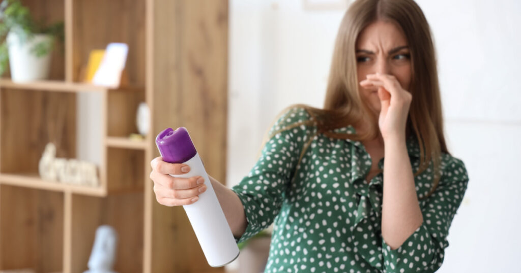 Displeased young woman with air freshener at home