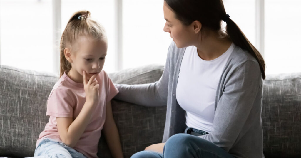 Serious mother talking to sad upset preschooler daughter kid at home. Mum consoling quiet girl, giving love, comfort, support, touching shoulder of child at home. Psychology, therapy, empathy concept