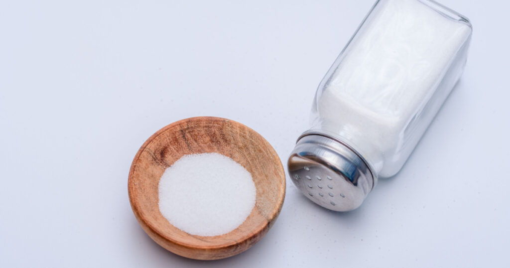 Salt shaker and salt in a wooden round bowl on a white background