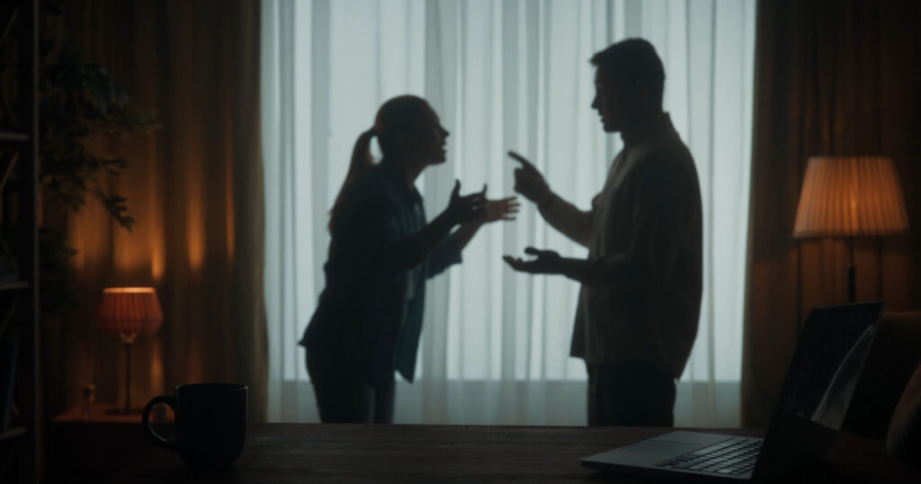A man and a woman are arguing in the living room near the window. A silhouette of a couple arguing over the fact that the man spends too much time on the laptop.
