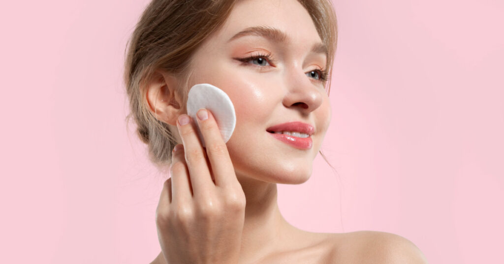 Beautiful woman removes make-up and cleanses her skin with cotton pads on a pink background