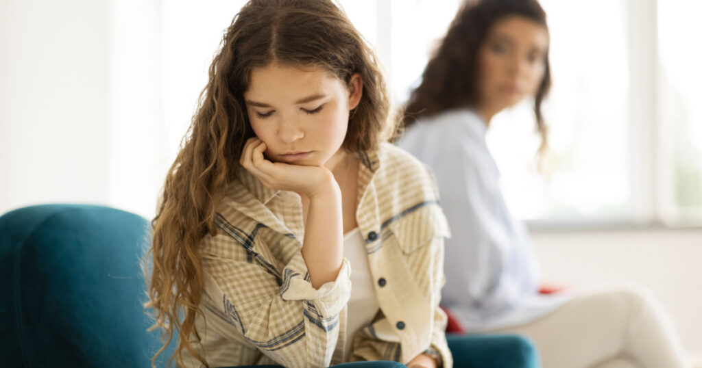 Unhappy offended caucasian teenager girl ignores adult mom after quarrel on sofa in living room interior. Problems in relationships at home, stress, break from negative emotions