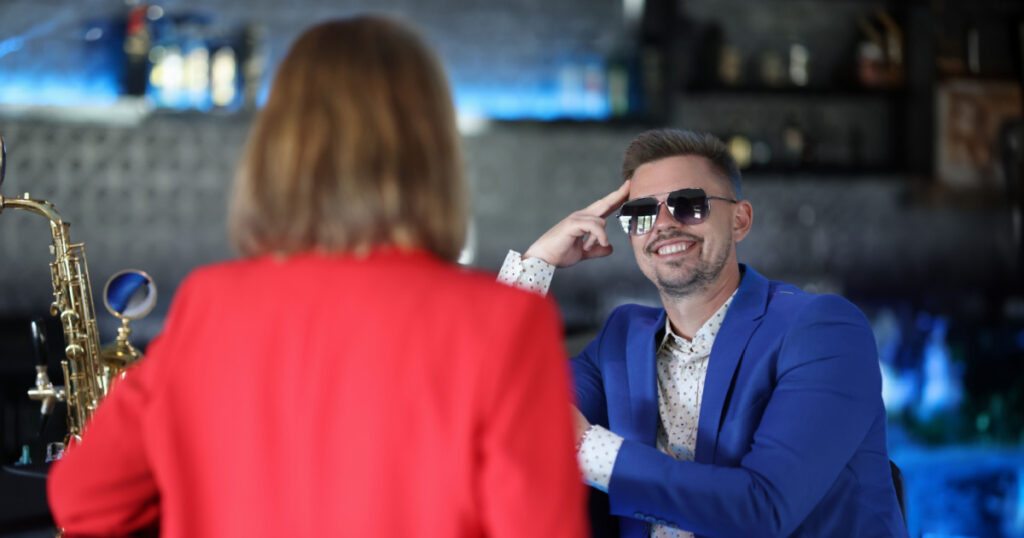 Smiling confident man in sunglasses meets woman near bar counter. Narcissistic personality disorder in men concept