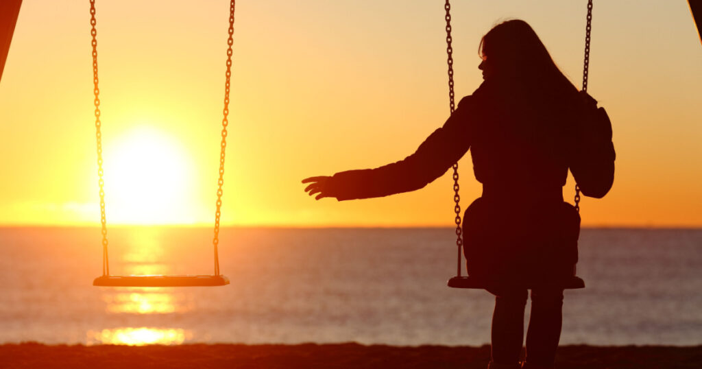 Single or divorced woman alone missing a boyfriend while swinging on the beach at sunset