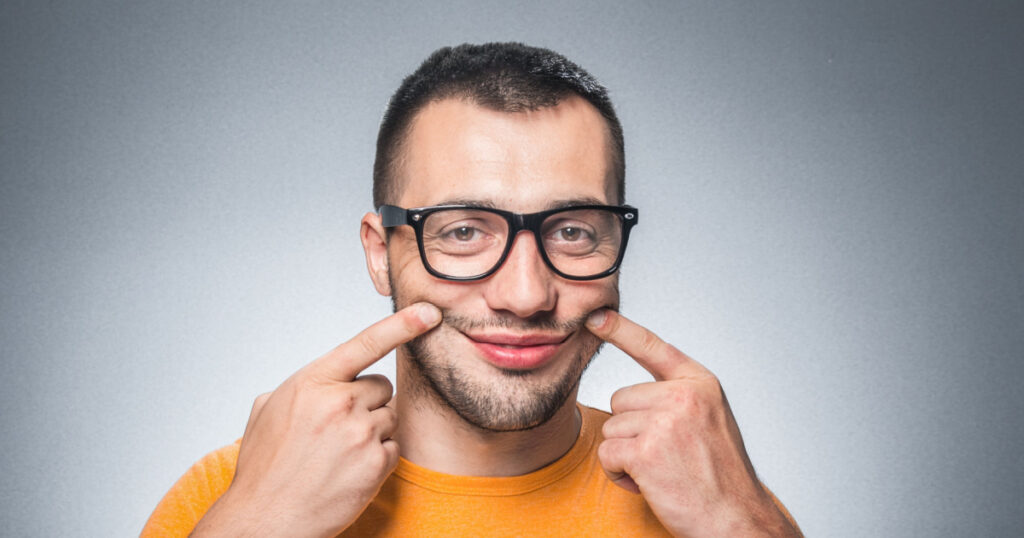 Fake smiling face, young man with fingers on his lips. Deceiver