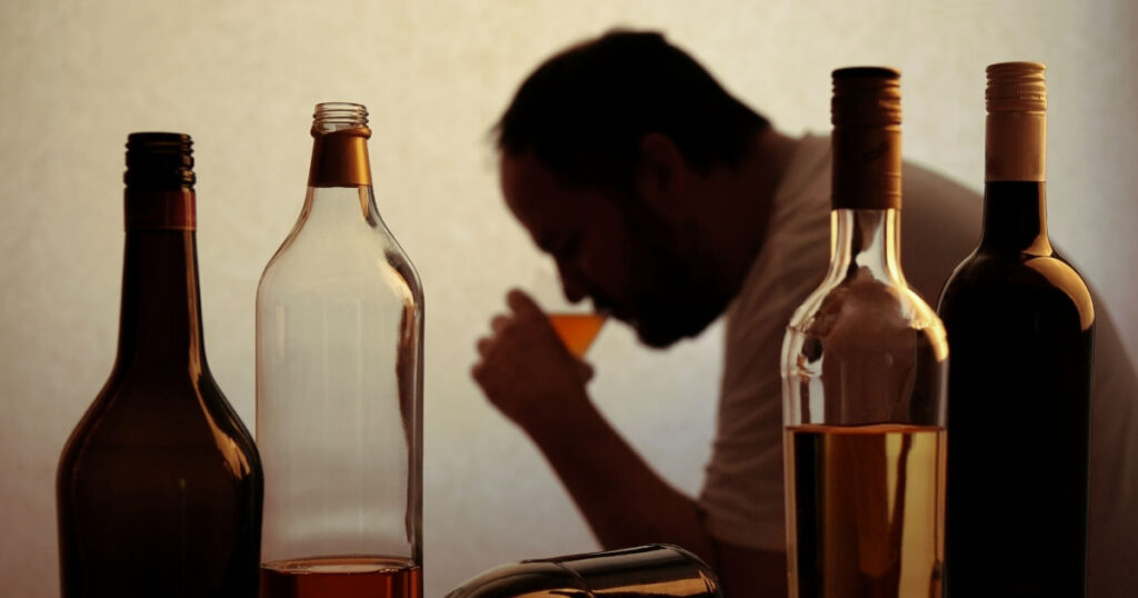 silhouette of anonymous alcoholic person drinking behind bottles of alcohol