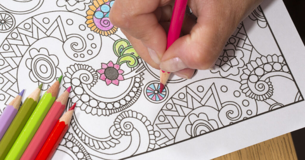 An image of a new trendy thing called adults coloring book. In this image a person is coloring an illustrative and detailed pattern for stress relieve for adults.