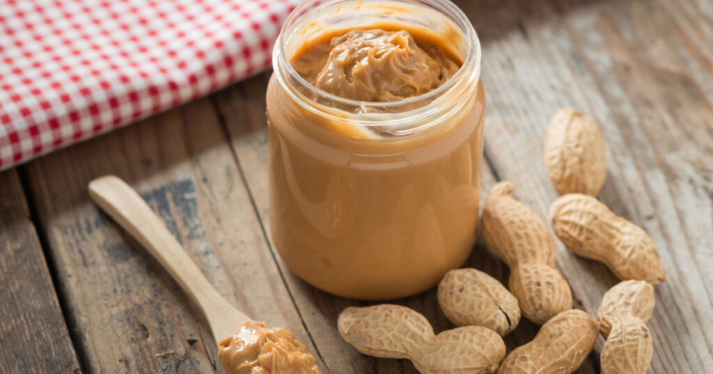 Creamy and smooth peanut butter in jar on wood table. Natural nutrition and organic food. Selective focus.