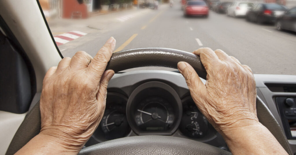 Senior woman driving a car on street in city.