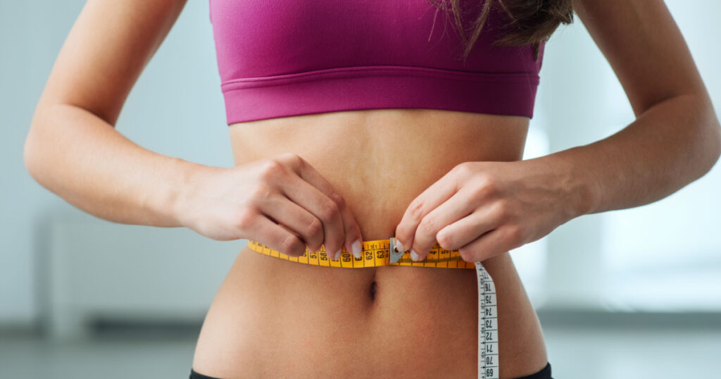 Slim young woman measuring her thin waist with a tape measure, close up