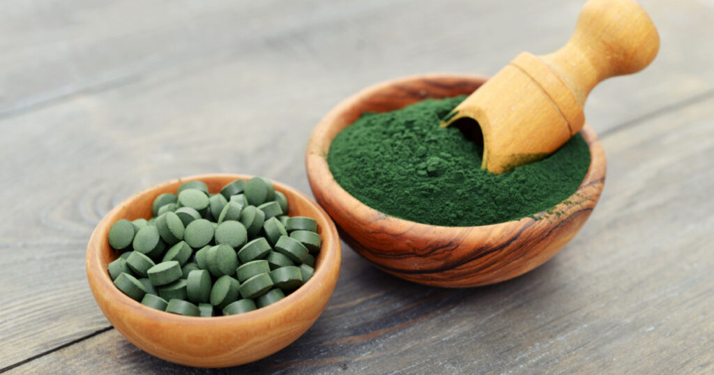 Ground spirulina and spirulina in pills over black wooden background