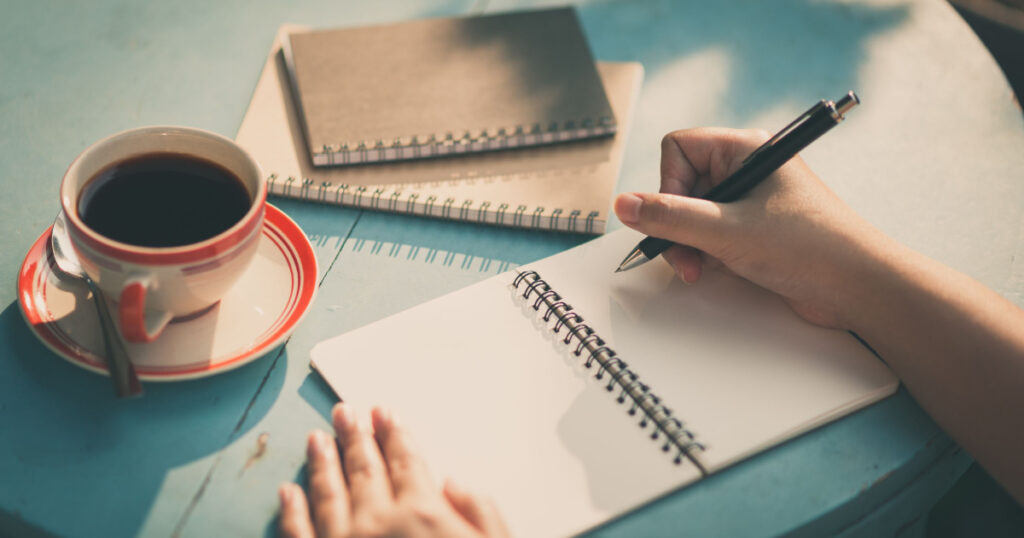 Woman right hand writing journal on small notebook at outdoor area in cafe with morning scene and vintage filter effect