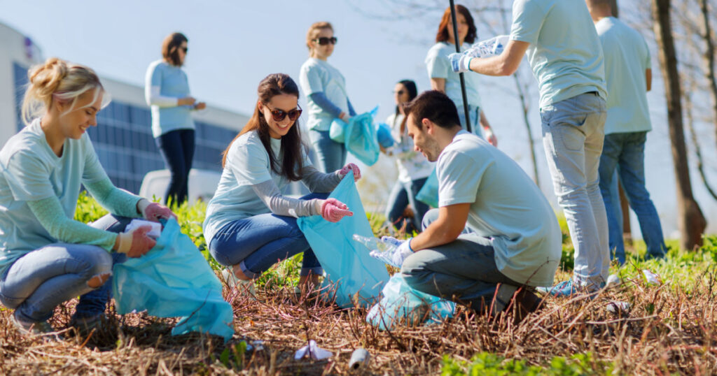 volunteering, charity, cleaning, people and ecology concept - group of happy volunteers with garbage bags cleaning area in park