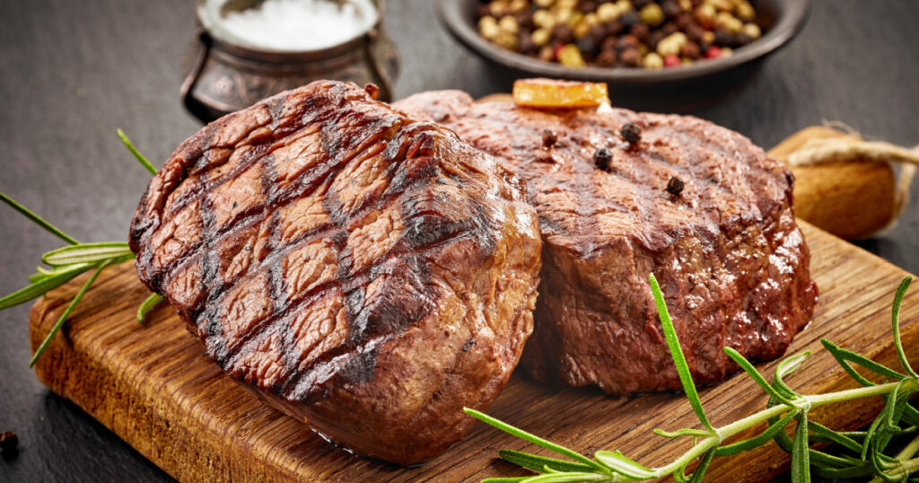 grilled beef steaks with spices on wooden cutting board