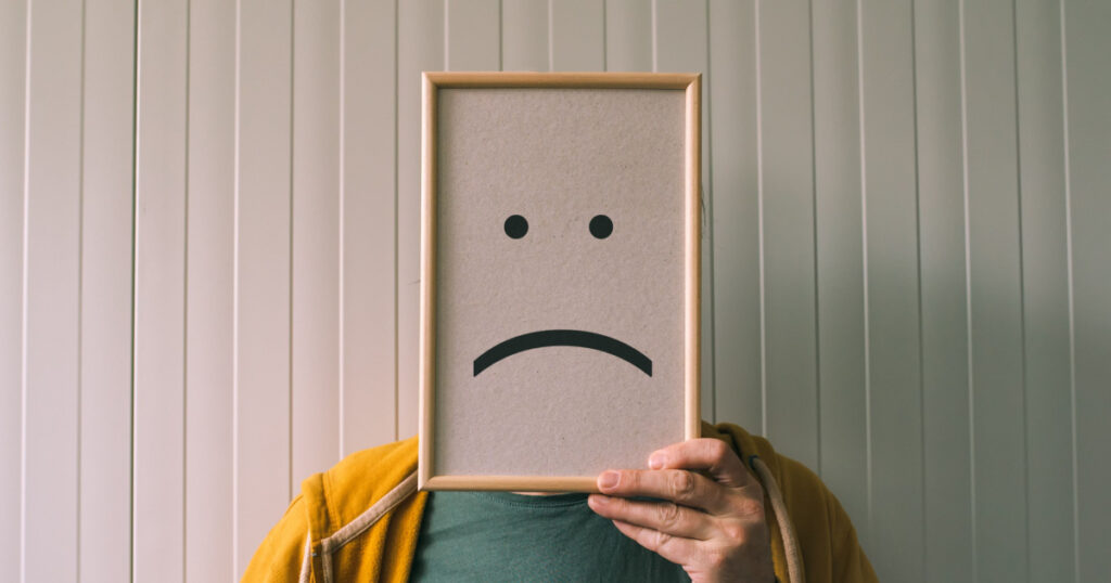 Put a sad pessimistic face on, sadness and depressive emotions concept, man holding picture frame with smiley emoticon printed.