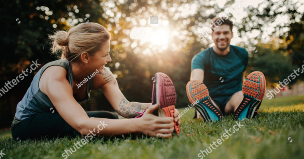 Fitness couple stretching outdoors in park. Young man and woman exercising together in morning.