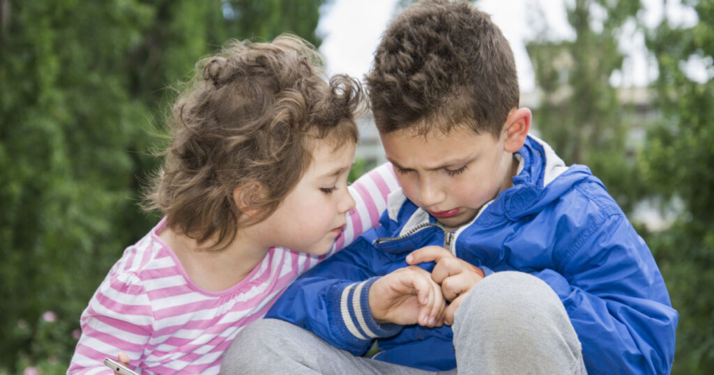 Summer in the park a little curly-haired boy shows his bad arm a little sister. She hugged him. Empathy regret it.