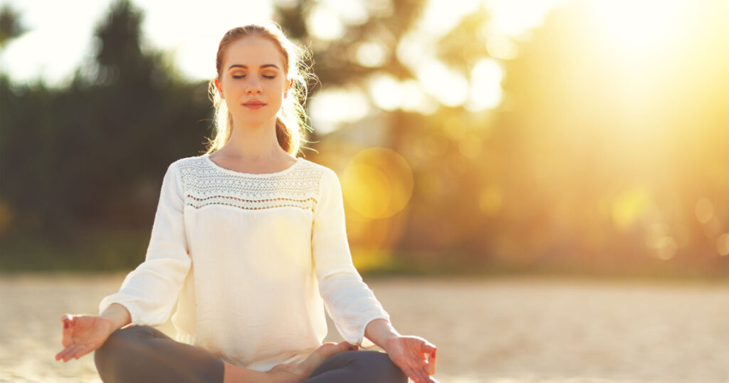 woman practices yoga and meditates in the lotus position on the beach