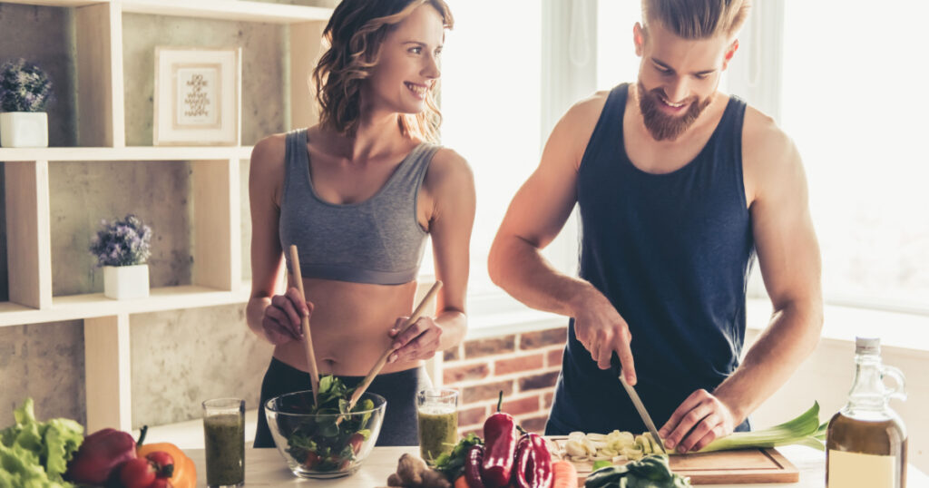 Beautiful young sports people are talking and smiling while cooking healthy food in kitchen at home