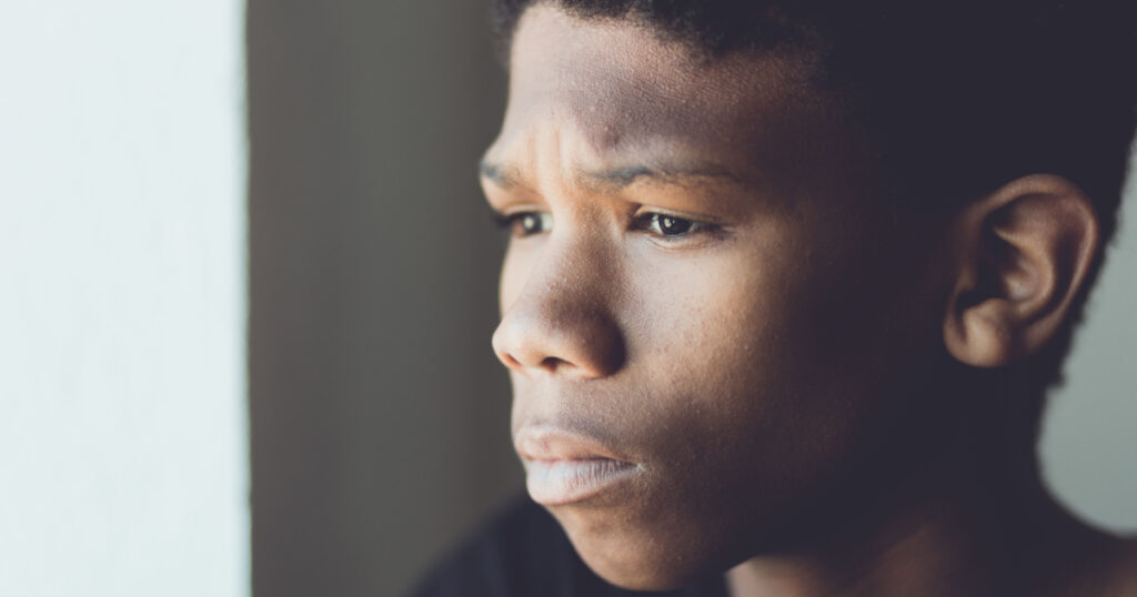 Faded retro portrait of a worried young African boy staring off to the side with a sad expression and frown in a close up side view