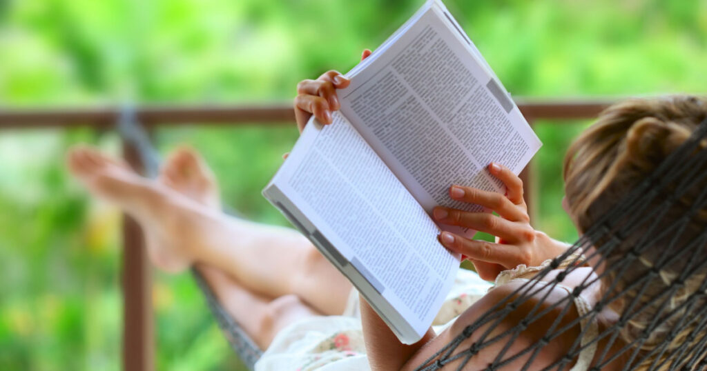 Young woman reading a book lying in hammock
