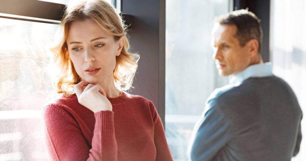 Problems in relationships. Sad unhappy cheerless woman standing near her boyfriend and holding her chin while feeling depressed