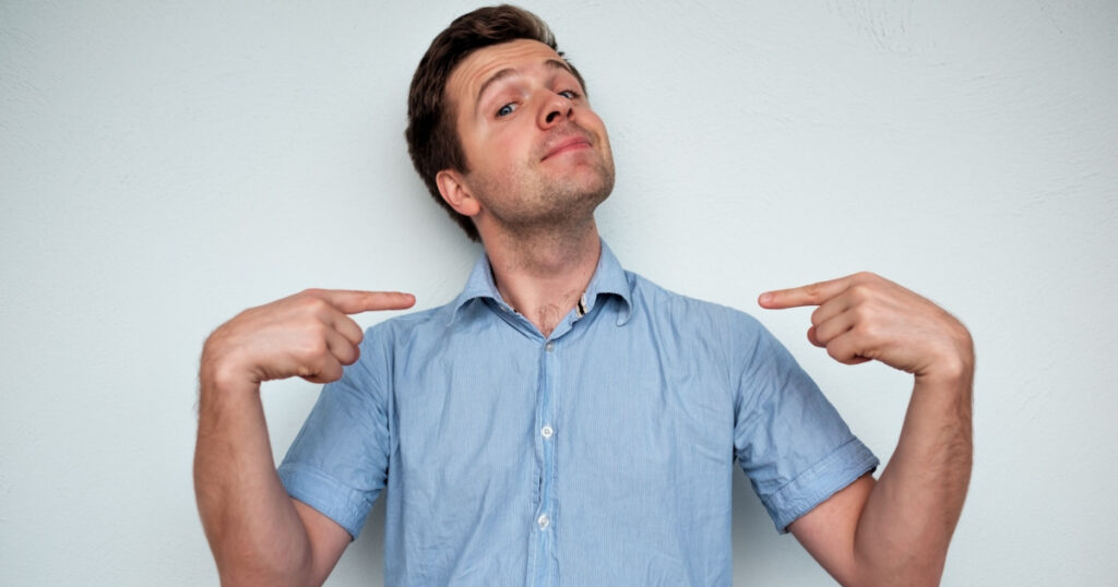 Self-satisfied and proud caucasian young man looks forward showing with index fingers on himself