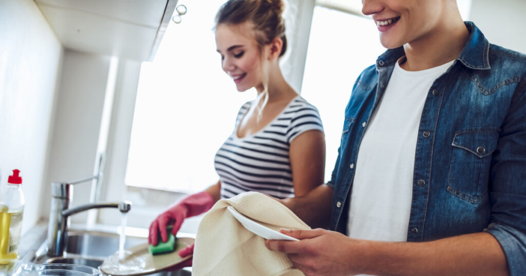 Cropped image of young happy couple is washing dishes while doing cleaning at home.