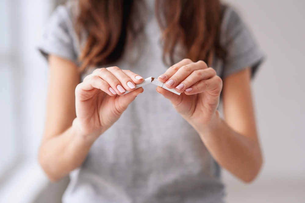 Stop smoking cigarettes concept. Portrait of beautiful smiling girl holding broken cigarette in hands. Happy female quitting smoking cigarettes. Quit bad habit, health care concept. No smoking.
