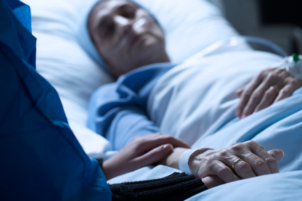 Young woman saying goodbye to her mother dying of cancer in a hospice, holding her hand