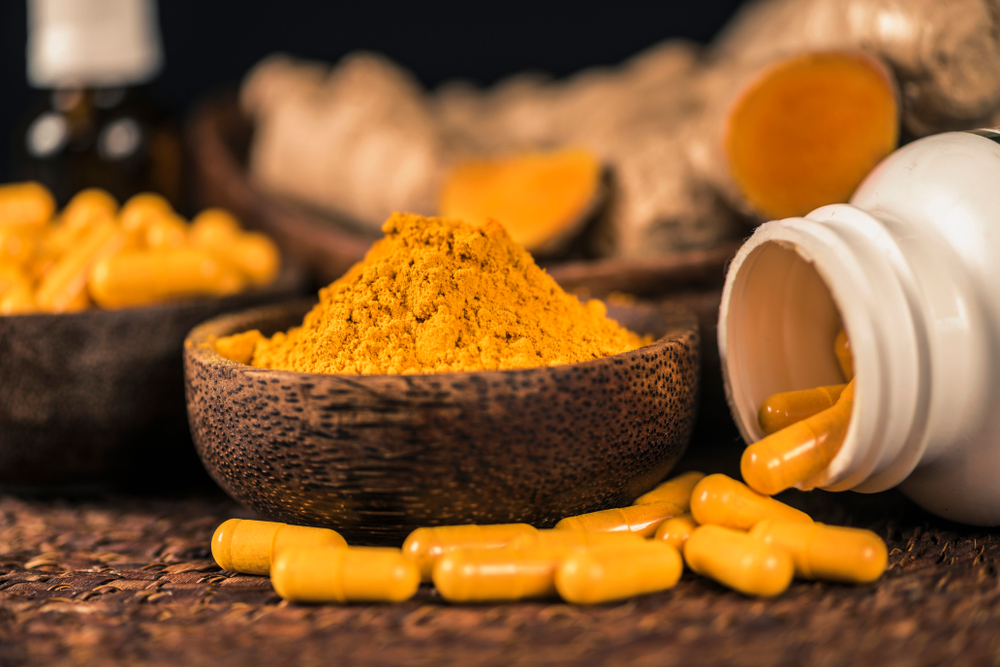 Curcumin supplement capsules, turmeric powder in glass bowl and curcuma root in background. Herbal medicine Curcuma against inflammation

