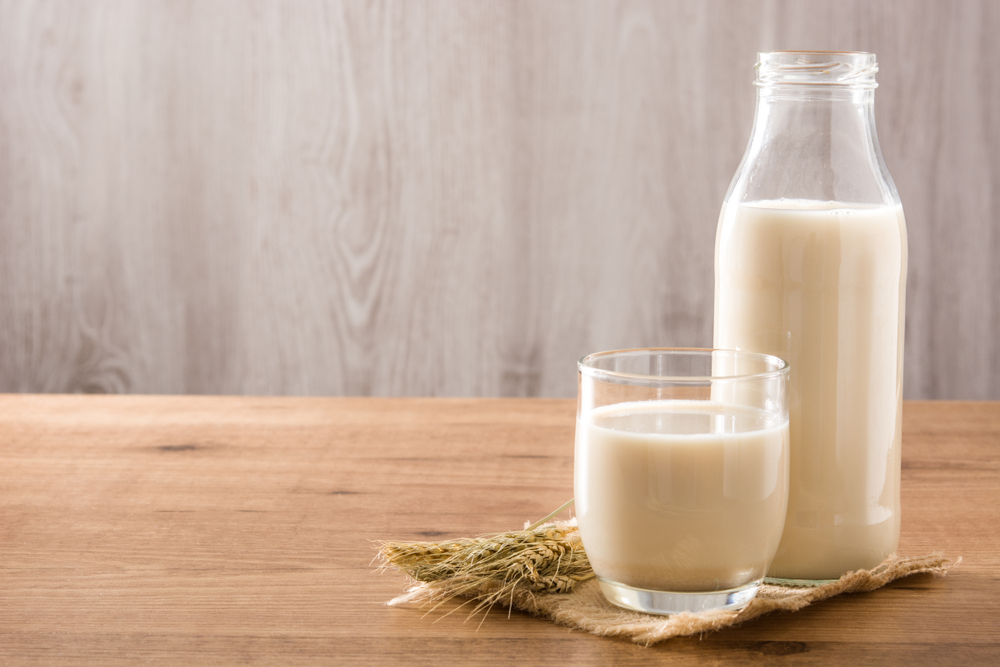 Oats milk in bottle and glass on wooden table. Copyspace