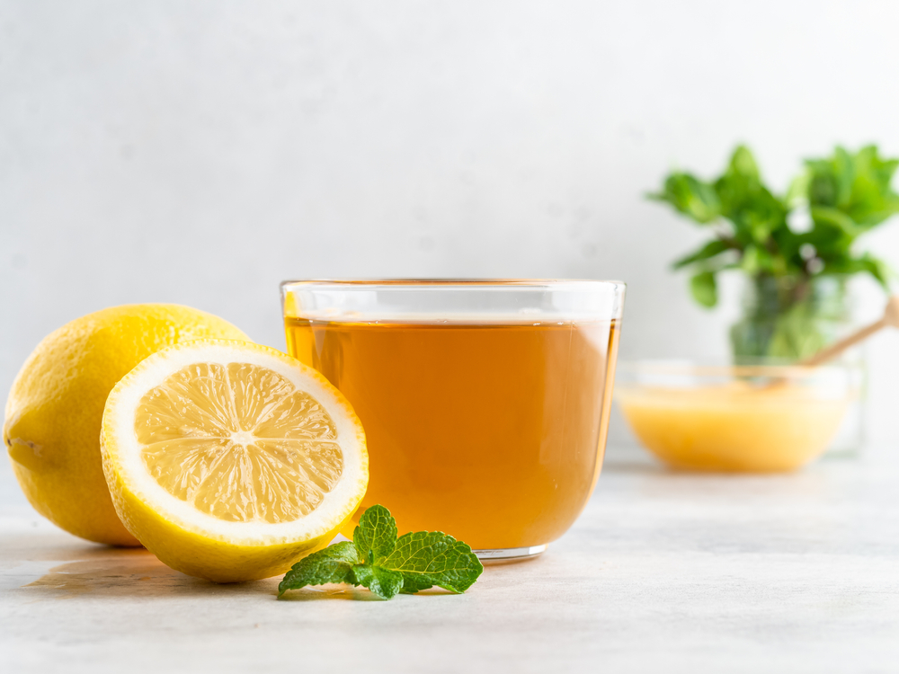 A glass cup of fresh green herbal tea with lemon, honey and green mint leaves. White background, close up view, copy space.
