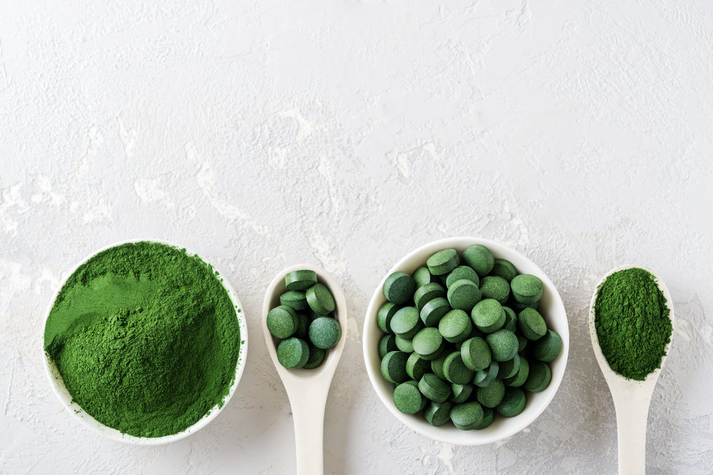 Chlorella or spirulina in the form of tablets and powder on a gray concrete background.
