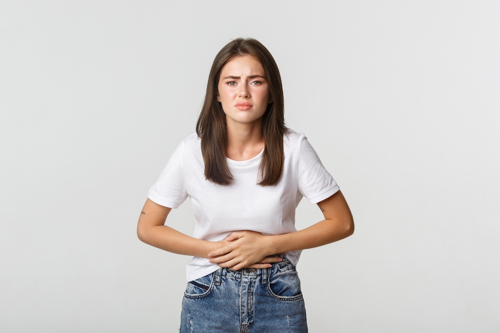 Woman having stomach ache, bending and holding hands on belly, discomfort from menstrual cramps. Girl feeling nauseous