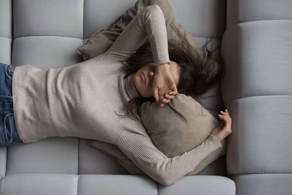 Peaceful pretty 20s girl lying on back on comfortable couch at home, covering eyes with hand, sleeping at daytime, feeling tired, enjoying relaxation, leisure, break, weekend. Top view

