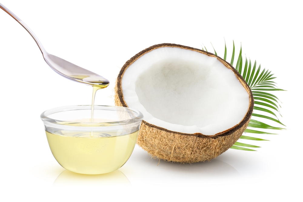 Coconut oil in glass bowl and coconut fruit with green leaves isolated on white background.