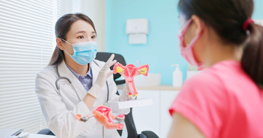 asian female doctor wear white coat and face mask explaining uterus model to woman in hospital
