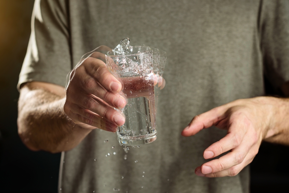 A man holds a glass of water with a shaking hand. The concept of parkinson's disease and tremor.
